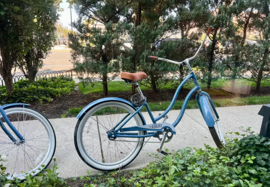 A blue bike and the wheel of another on a sidewalk.