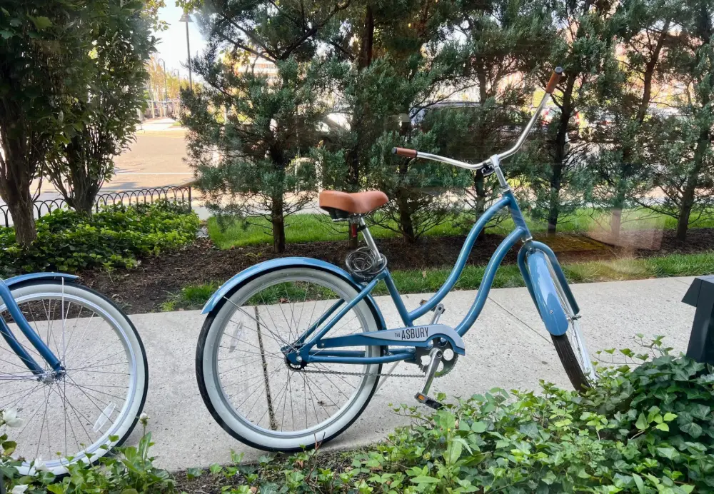 A blue bike and the wheel of another on a sidewalk.